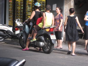 Familie på 4 på en scooter. Minstemannen stå fremst, de 2 andre ungene bak mora si.