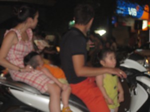 Familie på 4 på scooter. Minsten sover baki.